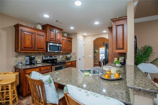 kitchen featuring stainless steel appliances, arched walkways, a peninsula, and tasteful backsplash