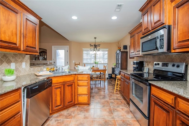 kitchen with brown cabinets, stainless steel appliances, visible vents, a sink, and a peninsula