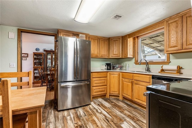 kitchen with light countertops, wood finished floors, freestanding refrigerator, and a sink