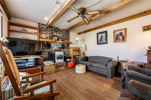 living area featuring visible vents, beam ceiling, a textured ceiling, wood finished floors, and ceiling fan