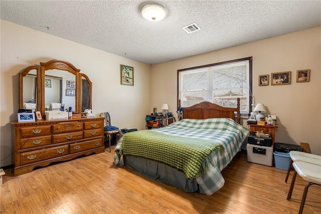 bedroom featuring visible vents, a textured ceiling, and wood finished floors