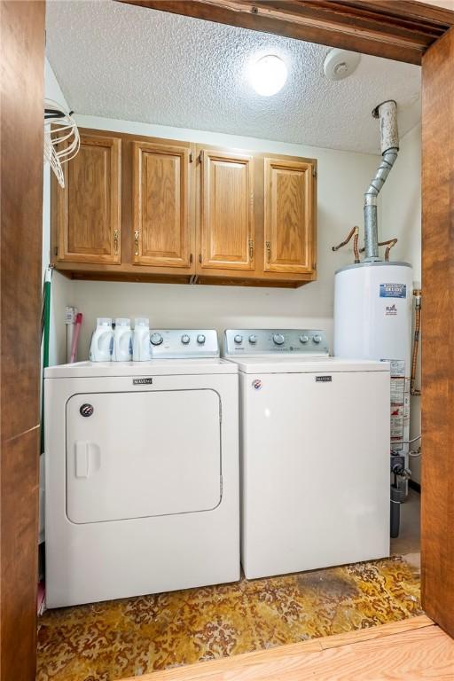 clothes washing area with a textured ceiling, gas water heater, cabinet space, and washing machine and clothes dryer