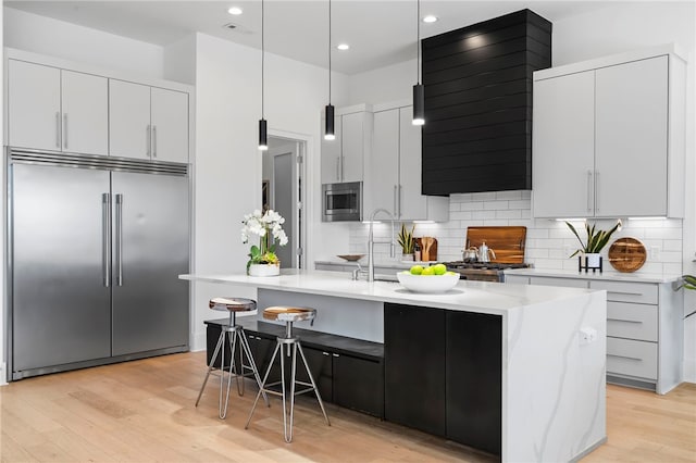 kitchen featuring light wood-style floors, tasteful backsplash, a kitchen island with sink, and built in appliances