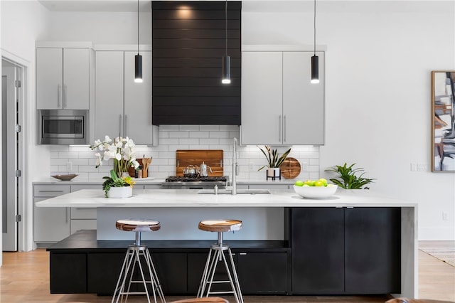 kitchen featuring backsplash, stainless steel microwave, a breakfast bar, and a sink