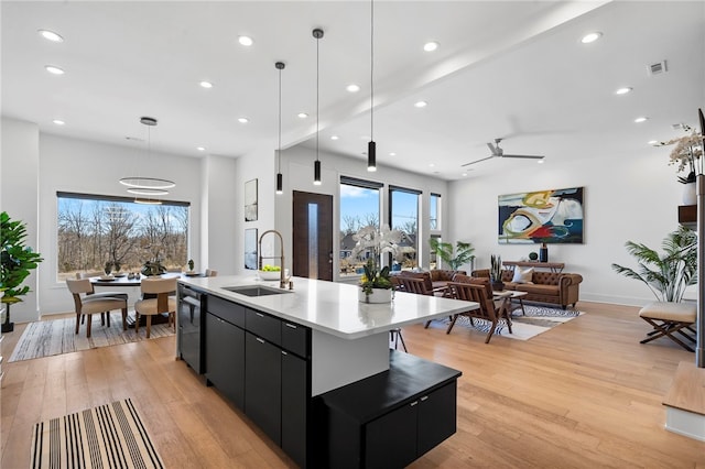 kitchen featuring visible vents, an island with sink, open floor plan, dark cabinets, and a sink