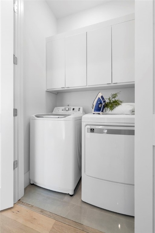 laundry area featuring light wood-type flooring, washing machine and clothes dryer, and cabinet space