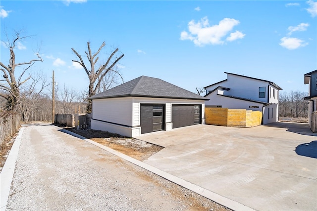 view of home's exterior with a garage, an outbuilding, roof with shingles, and fence