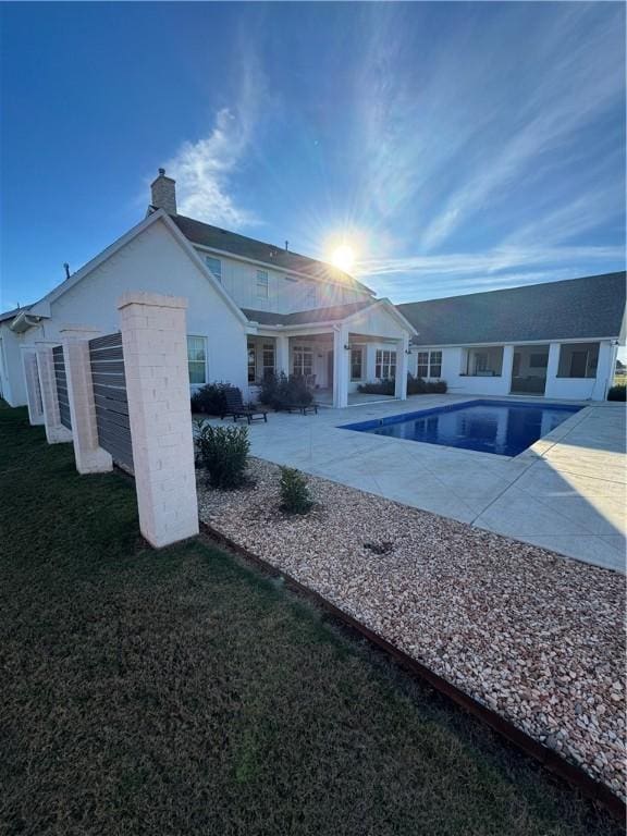 rear view of house with a yard, a chimney, concrete driveway, a patio area, and an outdoor pool