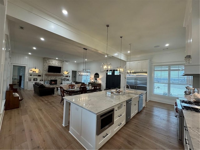 kitchen with a fireplace, open floor plan, white cabinets, wood finished floors, and built in appliances