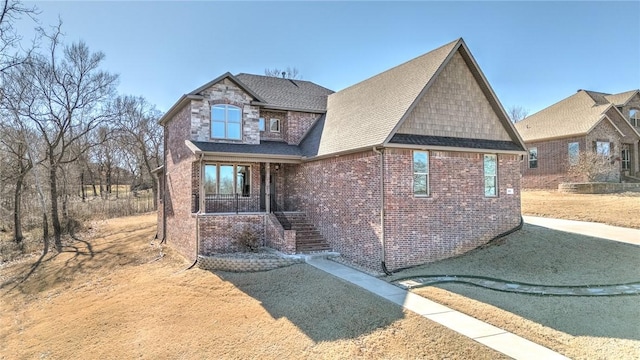 view of front of house with a shingled roof, stone siding, and brick siding