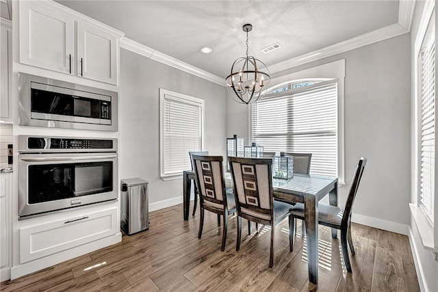 dining space featuring a notable chandelier, visible vents, crown molding, and wood finished floors