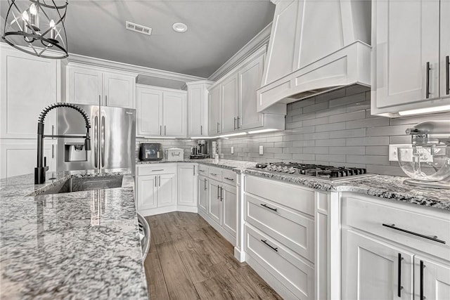 kitchen with custom exhaust hood, visible vents, white cabinetry, a sink, and wood finished floors