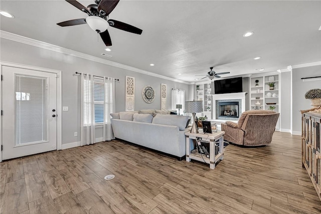 living room featuring a fireplace with raised hearth, ornamental molding, wood finished floors, and visible vents