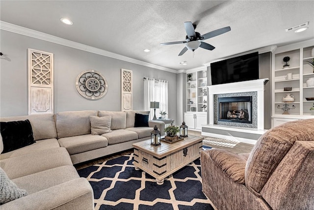 living room with a textured ceiling, a glass covered fireplace, visible vents, and crown molding