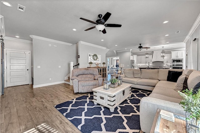 living room with baseboards, wood finished floors, visible vents, and crown molding