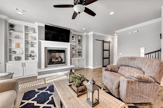 living area featuring crown molding, visible vents, a fireplace with raised hearth, a barn door, and wood finished floors