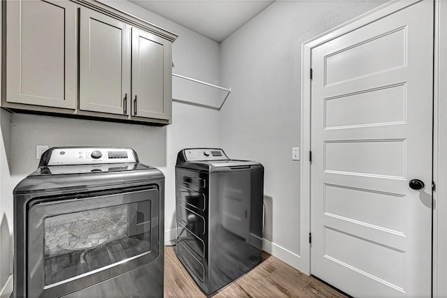 washroom featuring cabinet space, baseboards, light wood finished floors, and washing machine and clothes dryer