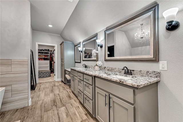 bathroom featuring wood finished floors, an inviting chandelier, double vanity, a sink, and a walk in closet