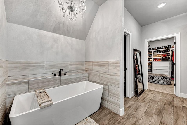 bathroom with wood finished floors, a spacious closet, a freestanding tub, a chandelier, and tile walls