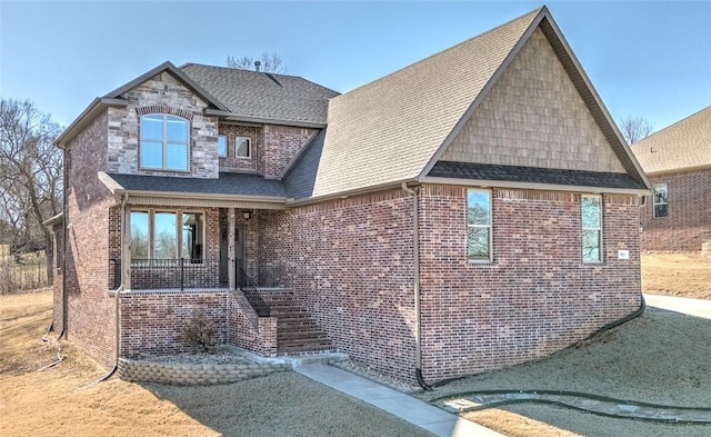 traditional home featuring stone siding, brick siding, a porch, and a shingled roof