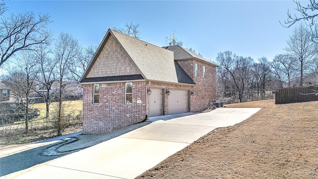 view of side of property featuring brick siding, roof with shingles, concrete driveway, an attached garage, and fence