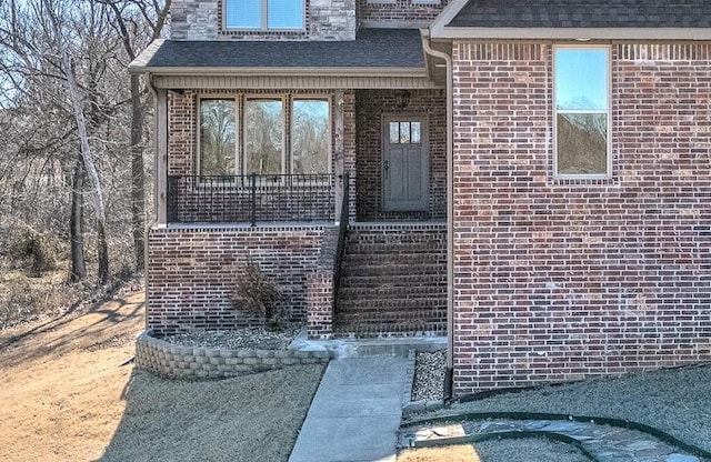 entrance to property with roof with shingles and brick siding