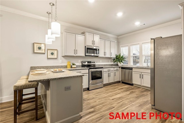 kitchen featuring a peninsula, a sink, appliances with stainless steel finishes, light wood-type flooring, and crown molding