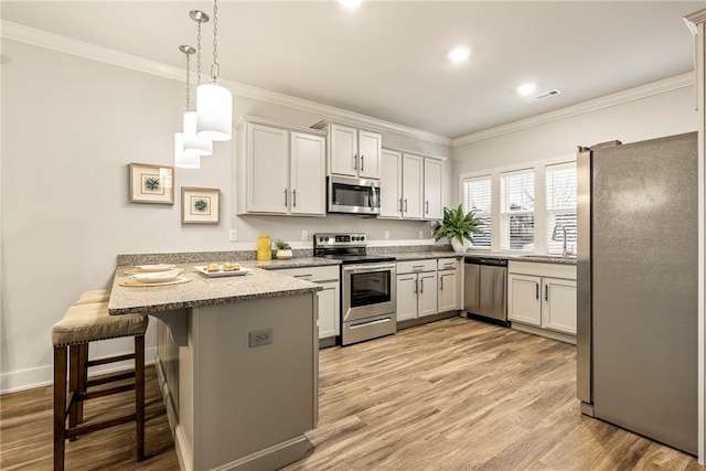 kitchen featuring appliances with stainless steel finishes, light wood-style floors, ornamental molding, a sink, and a peninsula