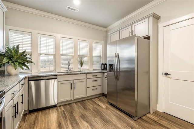 kitchen featuring dark wood-style floors, stainless steel appliances, visible vents, ornamental molding, and a sink