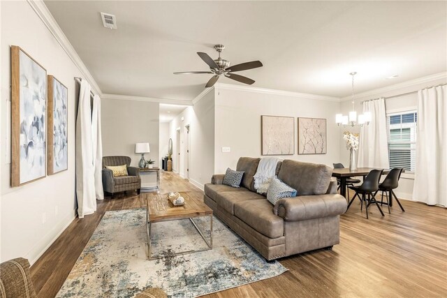 living area featuring visible vents, ornamental molding, wood finished floors, baseboards, and ceiling fan with notable chandelier