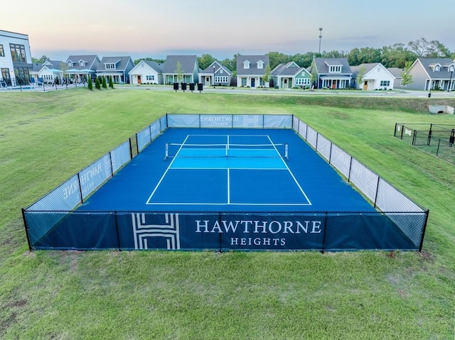 view of tennis court featuring a residential view, a lawn, and fence