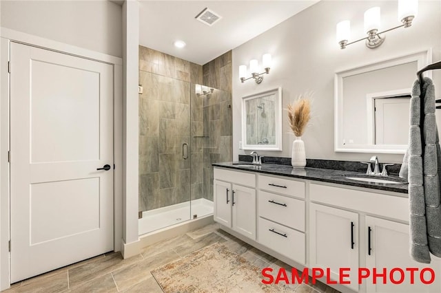 full bath featuring visible vents, a sink, a shower stall, and double vanity