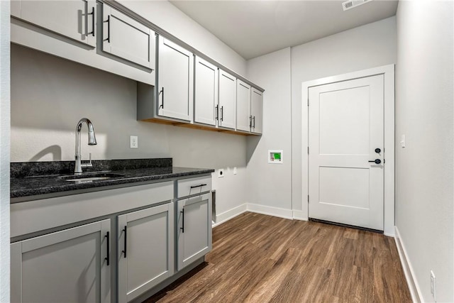 washroom featuring dark wood-style flooring, hookup for a washing machine, cabinet space, a sink, and baseboards