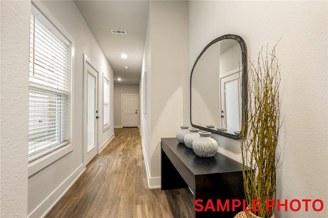 hallway with baseboards, visible vents, and wood finished floors