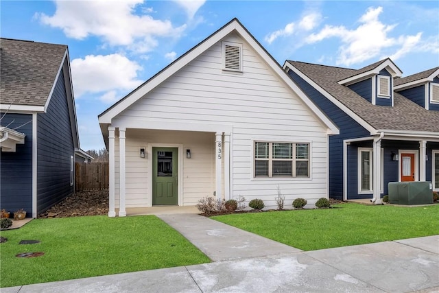 view of front of home with a shingled roof, a front lawn, and fence