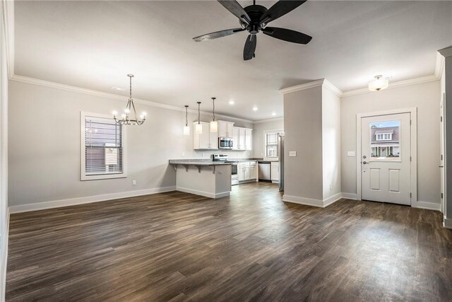 kitchen with a peninsula, appliances with stainless steel finishes, a breakfast bar area, and dark wood finished floors