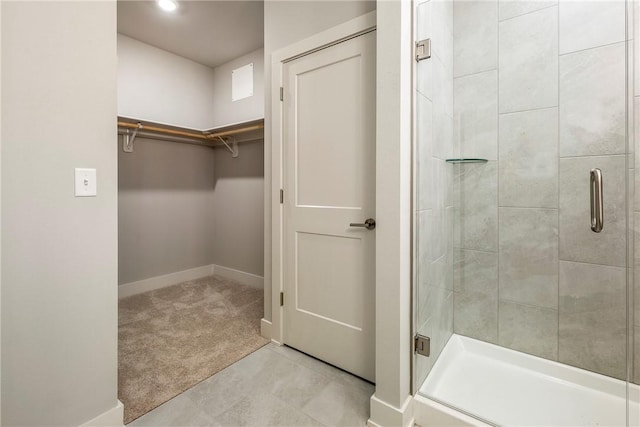 full bathroom with a walk in closet, a shower stall, and baseboards