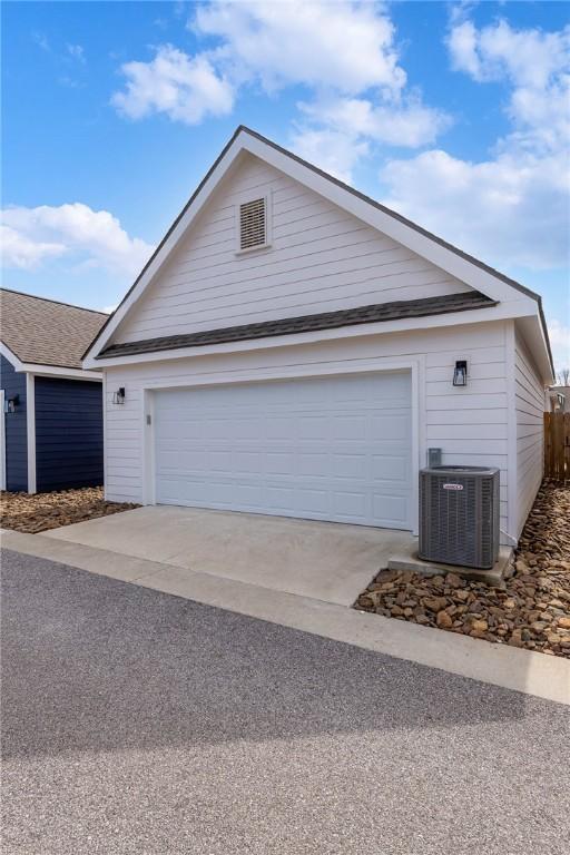 ranch-style house featuring cooling unit, roof with shingles, and concrete driveway