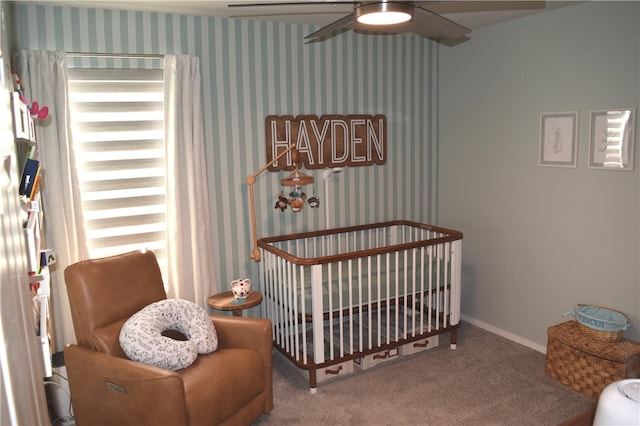 carpeted bedroom featuring a ceiling fan, a nursery area, baseboards, and wallpapered walls