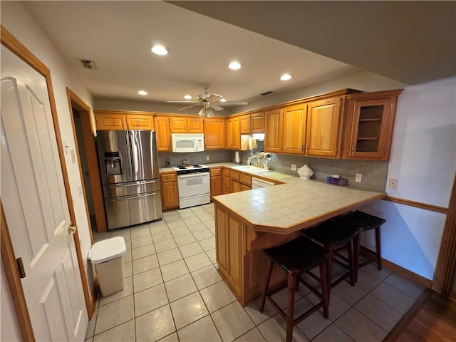 kitchen featuring tile counters, visible vents, backsplash, white appliances, and a peninsula