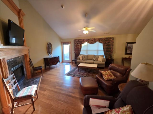 living area featuring a ceiling fan, lofted ceiling, a fireplace, and wood finished floors