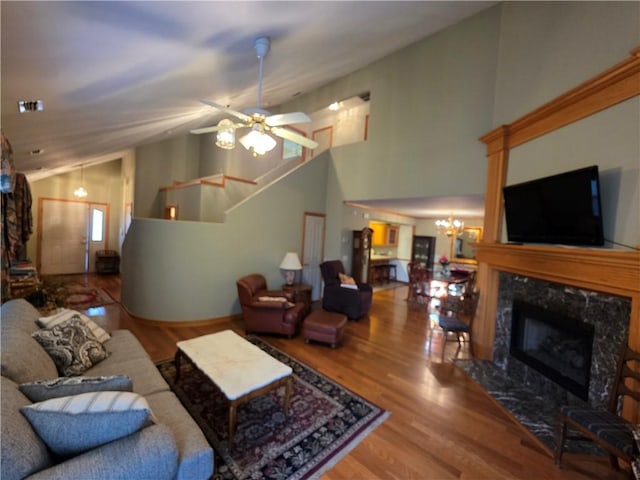 living room with a high end fireplace, lofted ceiling, wood finished floors, stairs, and ceiling fan with notable chandelier