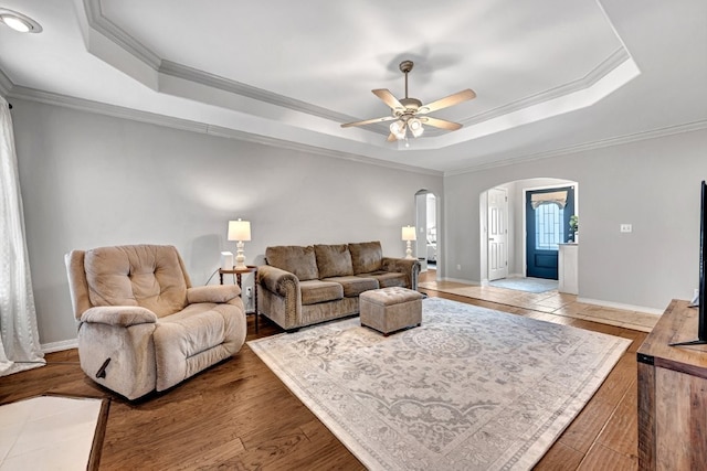 living area featuring arched walkways, a tray ceiling, wood finished floors, and ornamental molding