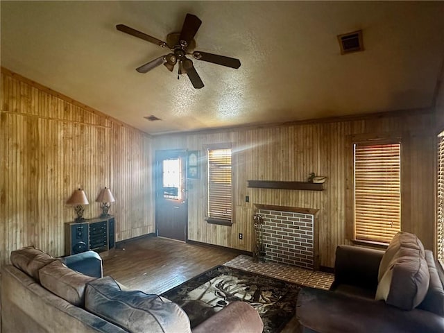 living room featuring visible vents, a fireplace with flush hearth, a ceiling fan, wooden walls, and wood finished floors