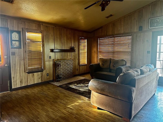 living area with visible vents, a ceiling fan, wood finished floors, vaulted ceiling, and a textured ceiling