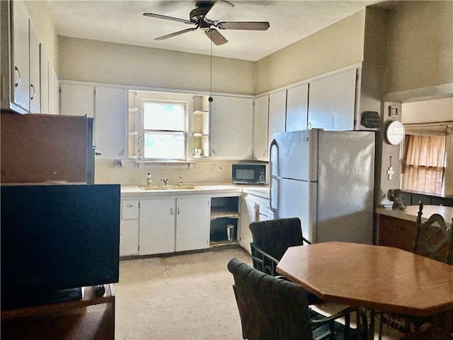 kitchen featuring light countertops, freestanding refrigerator, white cabinetry, a sink, and black microwave