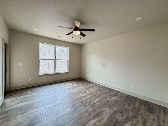 spare room featuring dark wood-style floors, ceiling fan, visible vents, and baseboards