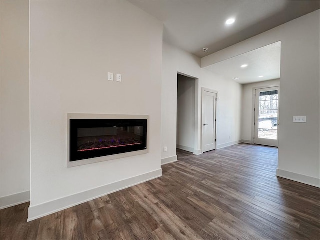 unfurnished living room with a glass covered fireplace, dark wood finished floors, baseboards, and recessed lighting