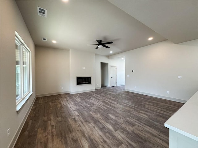 unfurnished living room featuring ceiling fan, recessed lighting, dark wood-type flooring, baseboards, and a glass covered fireplace