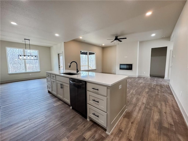 kitchen with dishwasher, a glass covered fireplace, dark wood-type flooring, a sink, and ceiling fan with notable chandelier